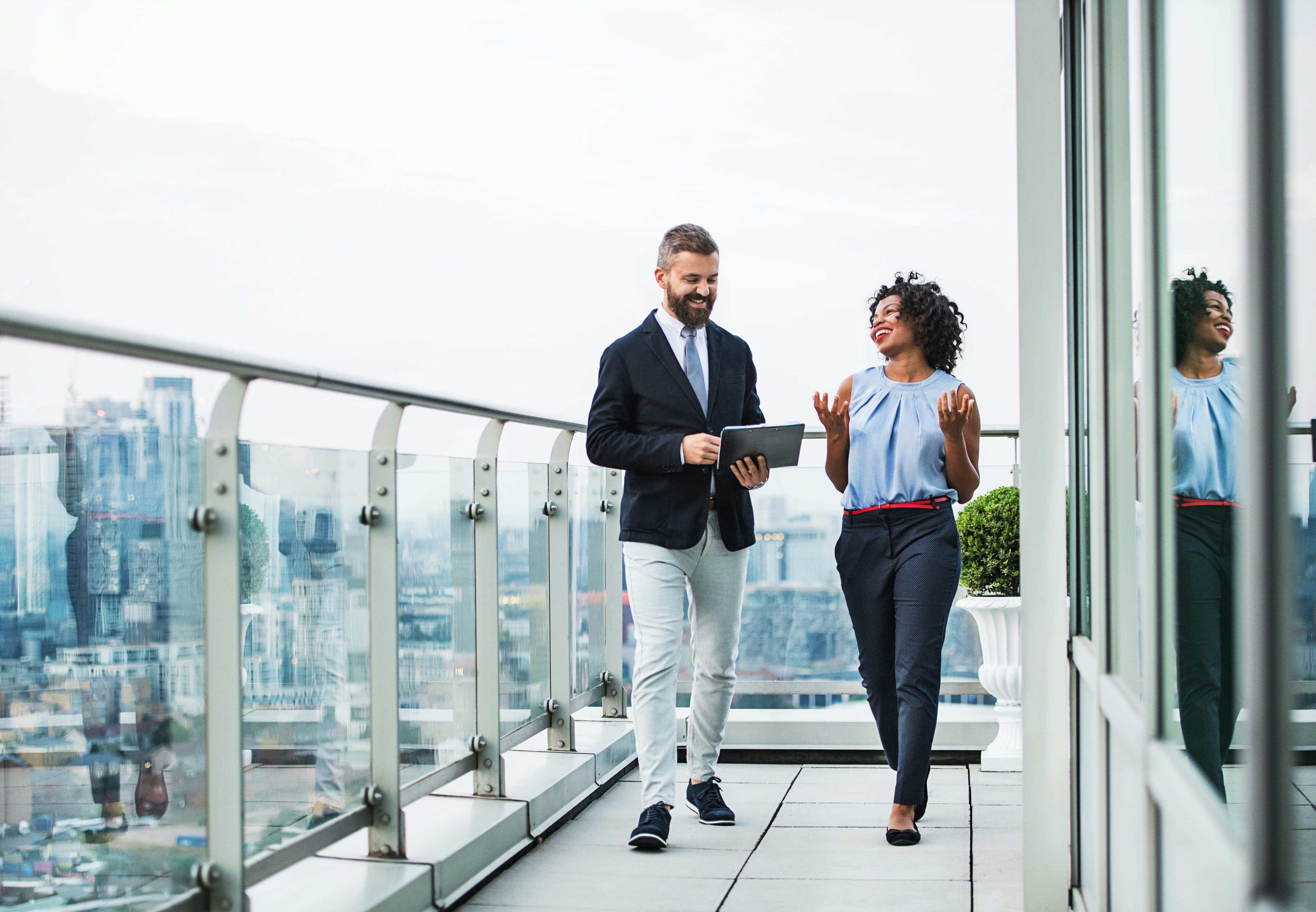 A woman and a man with a tablet having a conversation on a rooftop balcony